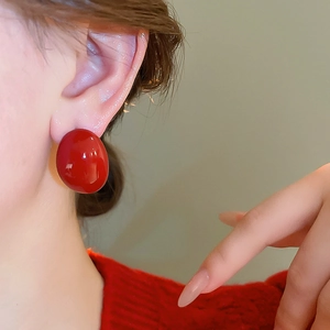 Close-up of model wearing deep red glossy stud earrings with minimalist round design