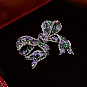 Close-up of silver bow brooch with purple marquise zircon and green crystals on red box