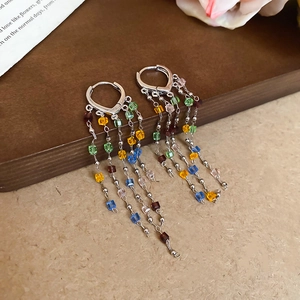 Macro detail of silver tassel earrings with colorful square crystals on dark wood surface
