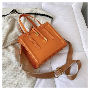 Detail view of bright orange square leather bag with wide strap on quilted fabric