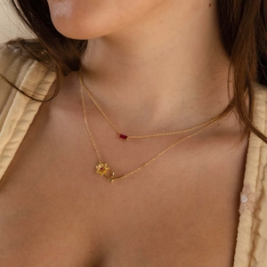 Gold double-layered necklace with flower pendant and red gemstone on a model
