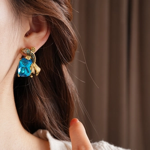 Macro detail of vintage fish-shaped earring with blue gem and diamonds on a model
