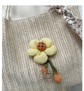 Close-up of beige straw tote bag featuring 3D yellow flower and printed silk scarf