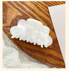 Close-up of white cloud-shaped acrylic hair claw clip on a circular wooden display tray