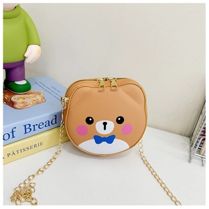 Detail of light brown bear shoulder bag with golden chain and blue bow tie on books