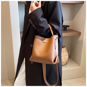 Detail of a brown leather bucket bag showing fine texture and MACGHEE logo on a model