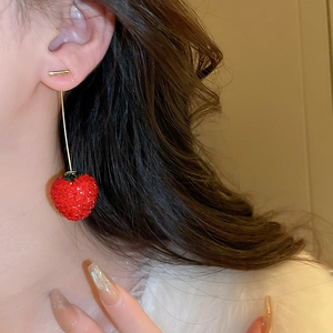Détail de boucles d'oreilles fraise rouges avec diamants portées par un mannequin