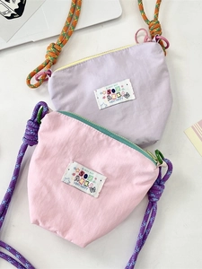 Pink and lilac crossbody phone bags with colorful braided straps on a white desk