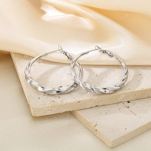 Close-up of silver twisted C-shape stainless steel earrings on a stone base with satin