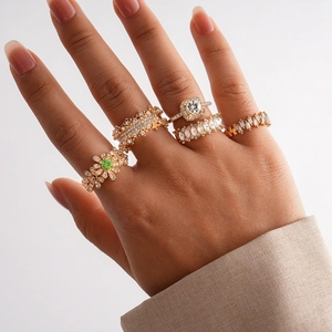 Detail of 5-piece gold ring set with green gems and square crystals on a hand
