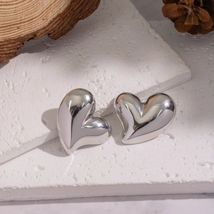 Polished silver heart-shaped stud earrings on a natural stone and rustic wooden background
