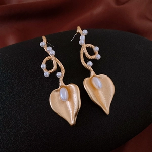 Detailed view of matte gold calla lily earrings with white pearls on silk background