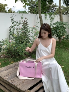Pink straw tote bag with black PARIS embroidery and white shoulder straps worn outdoors