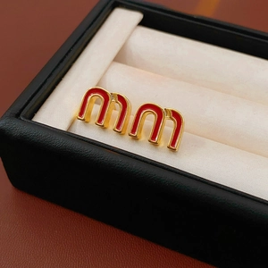 Detailed shot of red enamel and gold letter earrings on a white velvet jewelry box