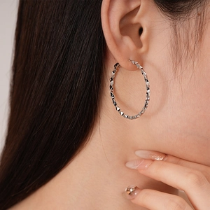 Silver geometric twisted hoop earrings with faceted design worn by a model