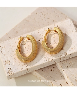 Macro shot of gold hoop earrings with grainy texture on beige stone blocks