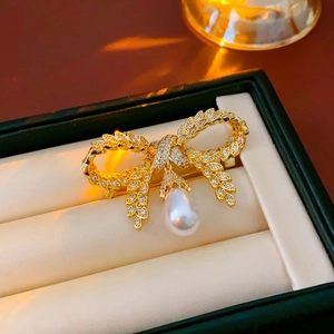 Détail d'une broche nœud dorée avec perle et zircons dans un écrin à bijoux élégant