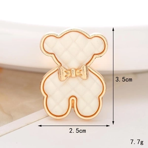 Detailed view of an ivory bear charm for clog shoes with gold trim and bow, size 3.5x2.5cm