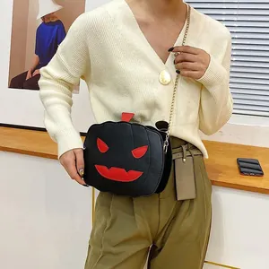 Detail of a black pumpkin-shaped crossbody bag with red face and gold chain strap
