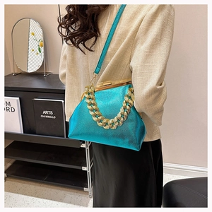 Detail of bright blue metallic handbag with thick gold chain strap on model's shoulder