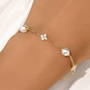 Detail of a gold clover bracelet with white pearls and sparkling zircons on white silk