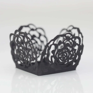 Macro detail of laser-cut black paper cupcake wrappers with delicate rose lace patterns