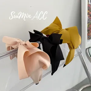 Three oversized bow headbands in beige black and yellow on a clear acrylic stand