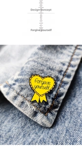 Detail of yellow heart enamel brooch with forgave yourself text on denim fabric