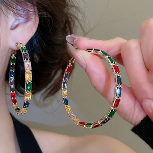 Macro shot of large golden hoop earrings featuring colorful rectangular zircon stones