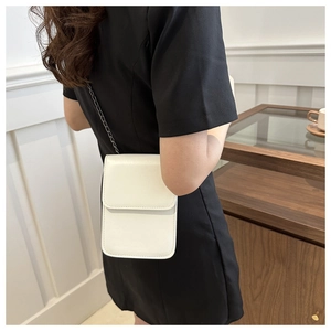 White minimalist mini crossbody phone bag with chain strap shown on person in a home setting