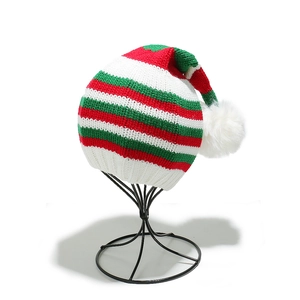 Macro view of red green and white striped Christmas knit hat with white fluffy pompom ball