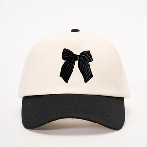 Dettaglio del cappello bicolore con corona crema e ricamo a fiocco nero sulla visiera