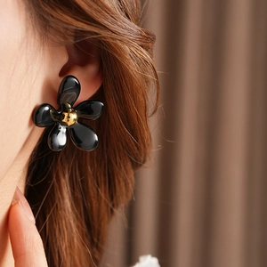 Close-up of elegant black flower earrings with gold center worn by a female model