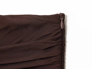 Detail of invisible zipper and pleated texture on dark brown semi-transparent dress