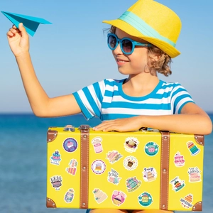 Kid with a vintage yellow suitcase decorated with colorful Happy Birthday stickers at the beach