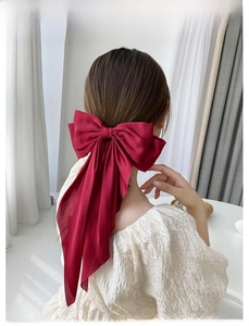 Detail of a large wine red satin bow hair clip with long ribbons worn on the back of the head
