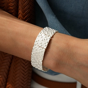 Détail d'un bracelet manchette argenté à motifs carrés porté sur le poignet