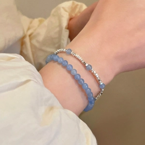 Détail de perles d'aigue-marine bleue et bracelets argentés superposés sur le poignet