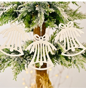 Three white glitter bell ornaments with bow detail hanging on a snowy Christmas tree