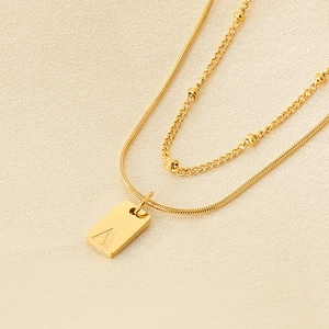 Detail einer doppelten Goldkette mit Schlangenkette und rechteckigem Anhänger mit Gravur A