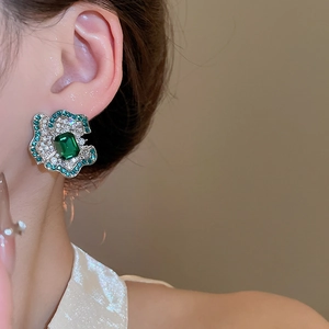 Macro shot of a floral earring with emerald-cut green stone and sparkling micro-inlay petals