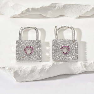 Detailed close-up of silver padlock earrings with micro-paved gems and red heart center