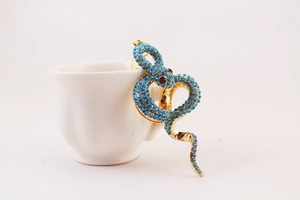 Detailed view of a golden snake ear cuff with blue rhinestones on a white cup handle