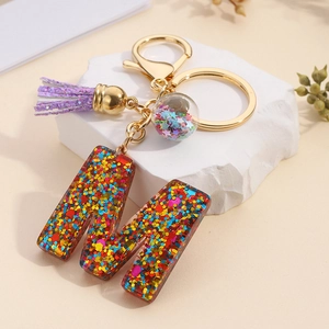 Macro detail of letter M resin keychain with colorful sequins and purple glitter tassel