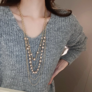 Detail of layered gold metal chain necklace with faux pearls worn on a grey sweater