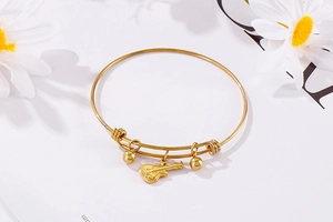 Detailed shot of a gold guitar charm and beads on a sleek stainless steel bangle