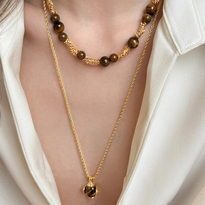 Collana a strati dorata con perline occhio di tigre e ciondolo rotondo su modella
