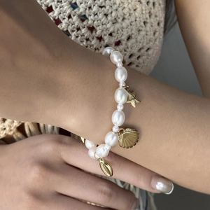 Detail of bohemian pearl bracelet with gold starfish and seashell charms on wrist