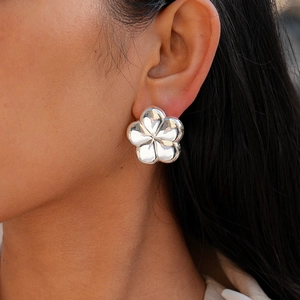 Detailed close-up of polished silver flower stud earrings on a model with mirror finish