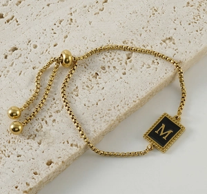 Détail d'un bracelet gourmette dorée réglable avec un pendentif lettre M en émail noir